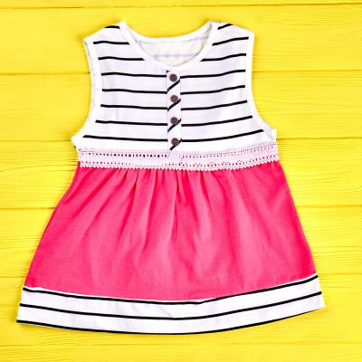 Baby-girl modern summer dress. Infant girl sleeveless sundress on yellow wooden background. Kids brand apparel on sale.